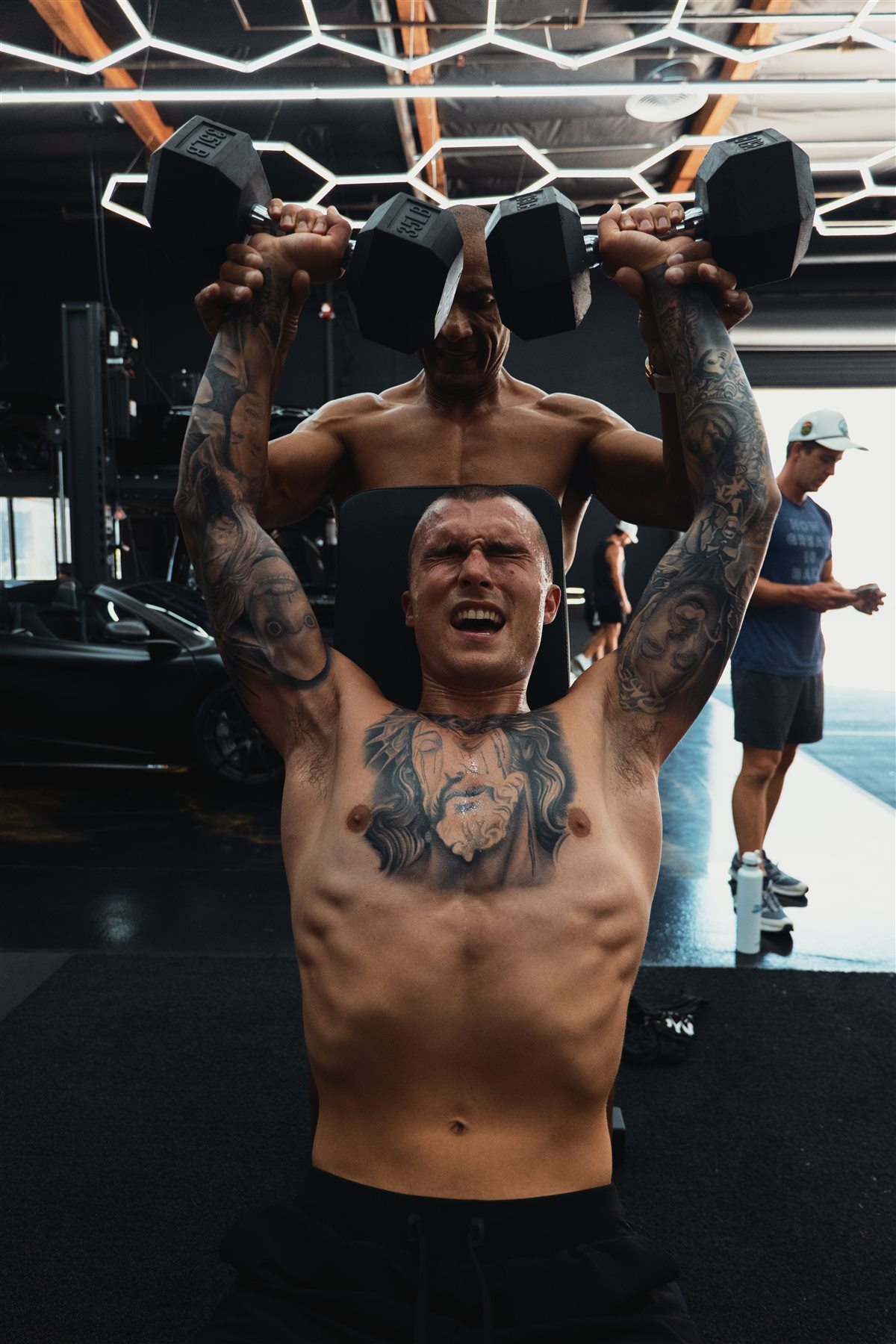 One member supporting another through a demanding dumbbell press