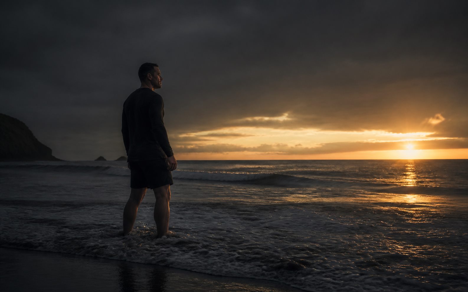 A man stepping deliberately into cold ocean surf at first light